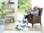 Älterer Mann sitzt im Sessel im Wohnzimmer und trainiert mit den Beinen am Bewegungstrainer Tigo