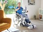 Mann sitzt im Wohnzimmer im Rollstuhl und trainiert mit dem Armen am Bewegungstrainer Tigo