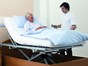 Mann sitzt in seinem Pflegebett und lächelt Pfleger an - Bett-im-Bett System Belluno